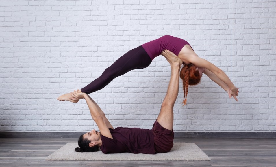 Flyer in Whale Pose supported by the Base’s feet, arching backward like on a hammock